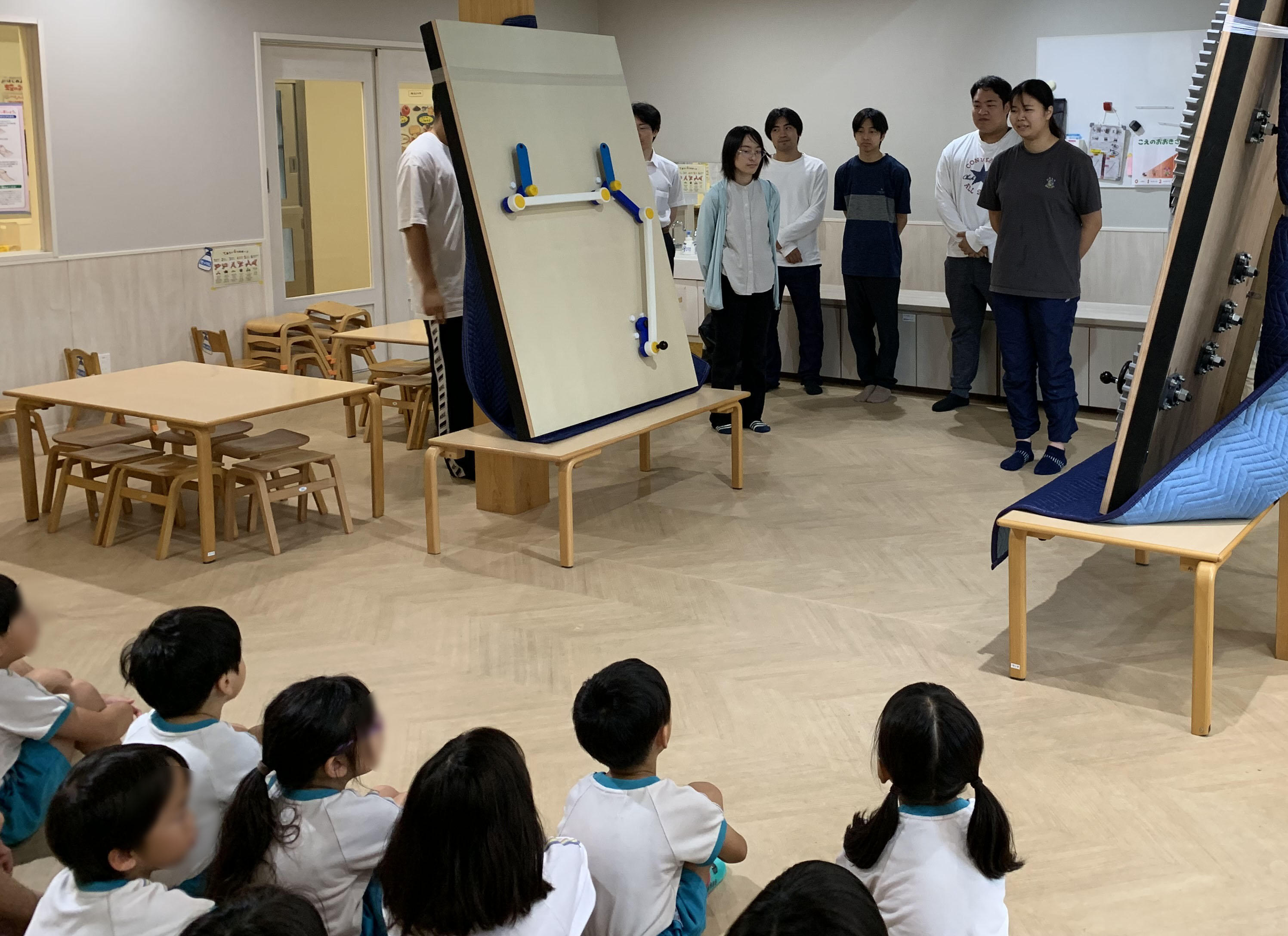 ひろかわ幸輪保育園の体験会で、学生たちが持ち込んだ試作品の装置を囲んで、興味深く触り始める園児たちの様子