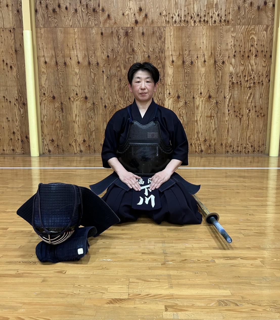 剣道の防具を身につけ、静かに正座をする久留米工業大学の下川美佳准教授。日本代表コーチも務めるトップ指導者としての風格が漂う一枚。