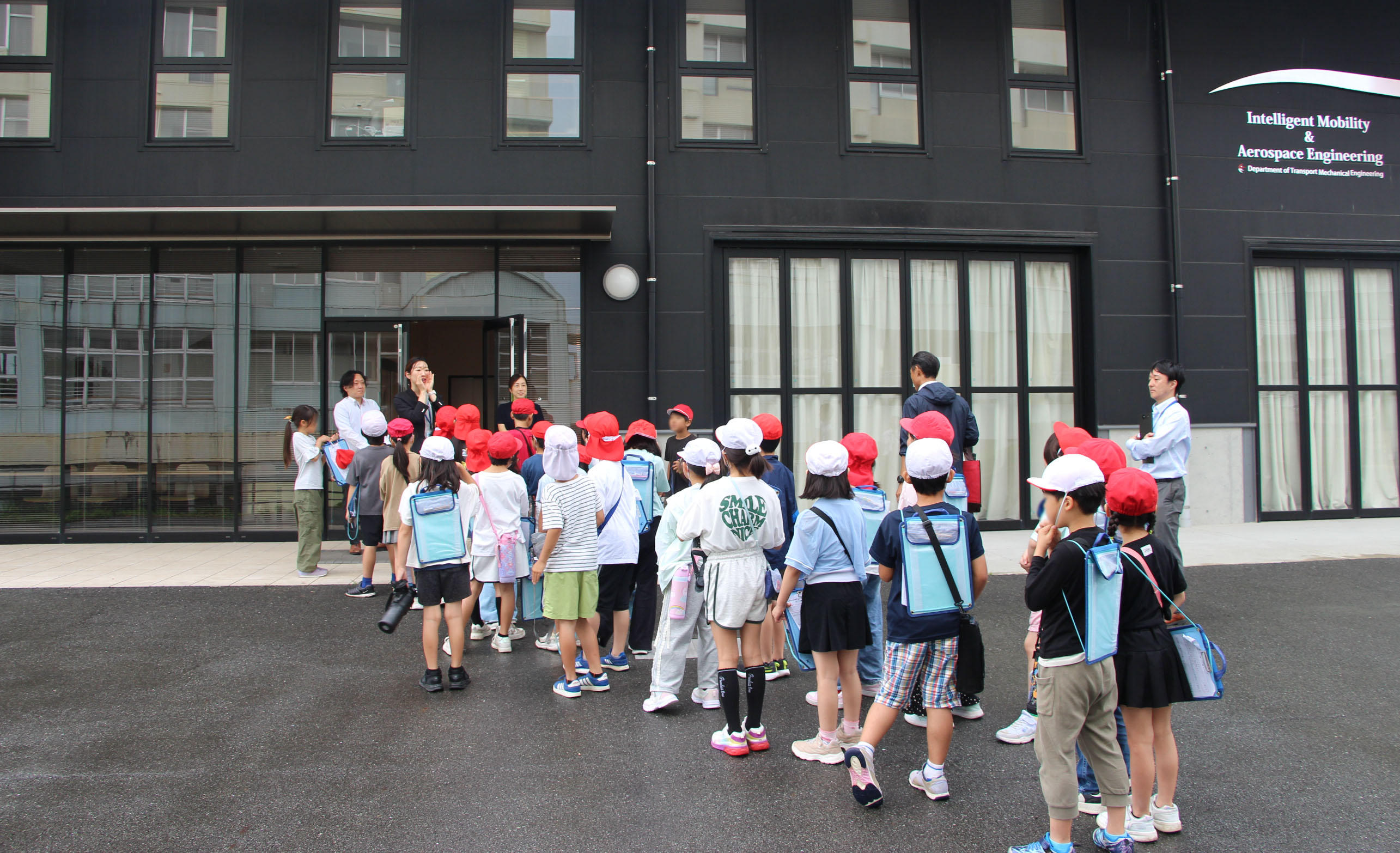 久留米市立上津小学校3年生の児童たちが社会科見学のため、久留米工業大学のキャンパスに来学し、青空のもと並んで歩いている様子。