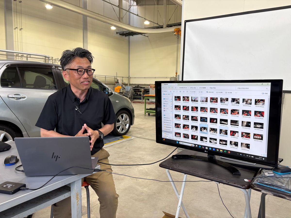 久留米工業大学の梶山助教が、パソコンモニターに映した設計図を指し示しながら、学生たちと展示物の構造について詳細な打ち合わせを行っている様子。