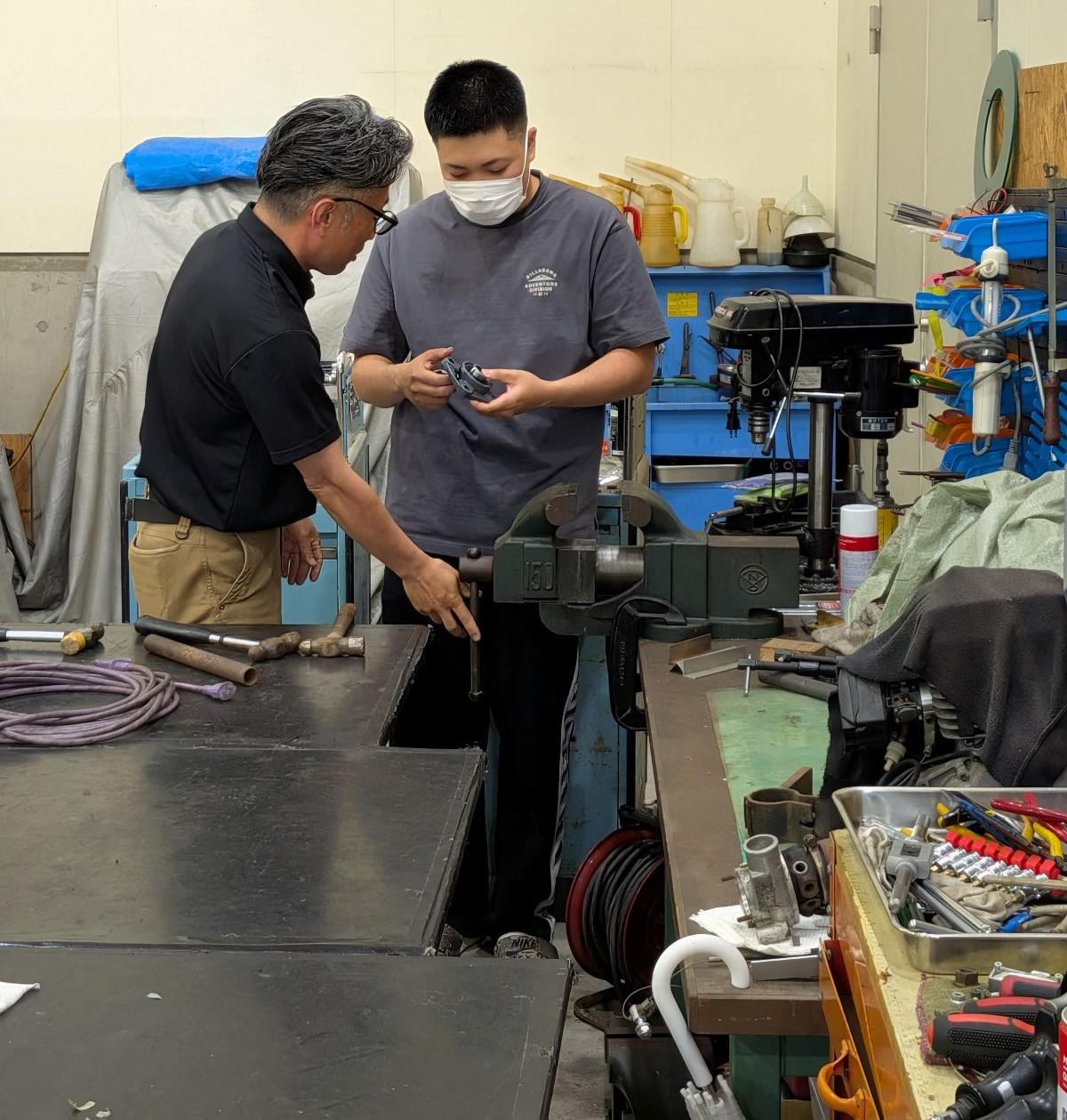 久留米工業大学の実験棟において、梶山助教が大学院生の藤本さんに対し、プロの精密加工業者へ依頼するための設計上の注意点や安全性について直接指導を行っている様子