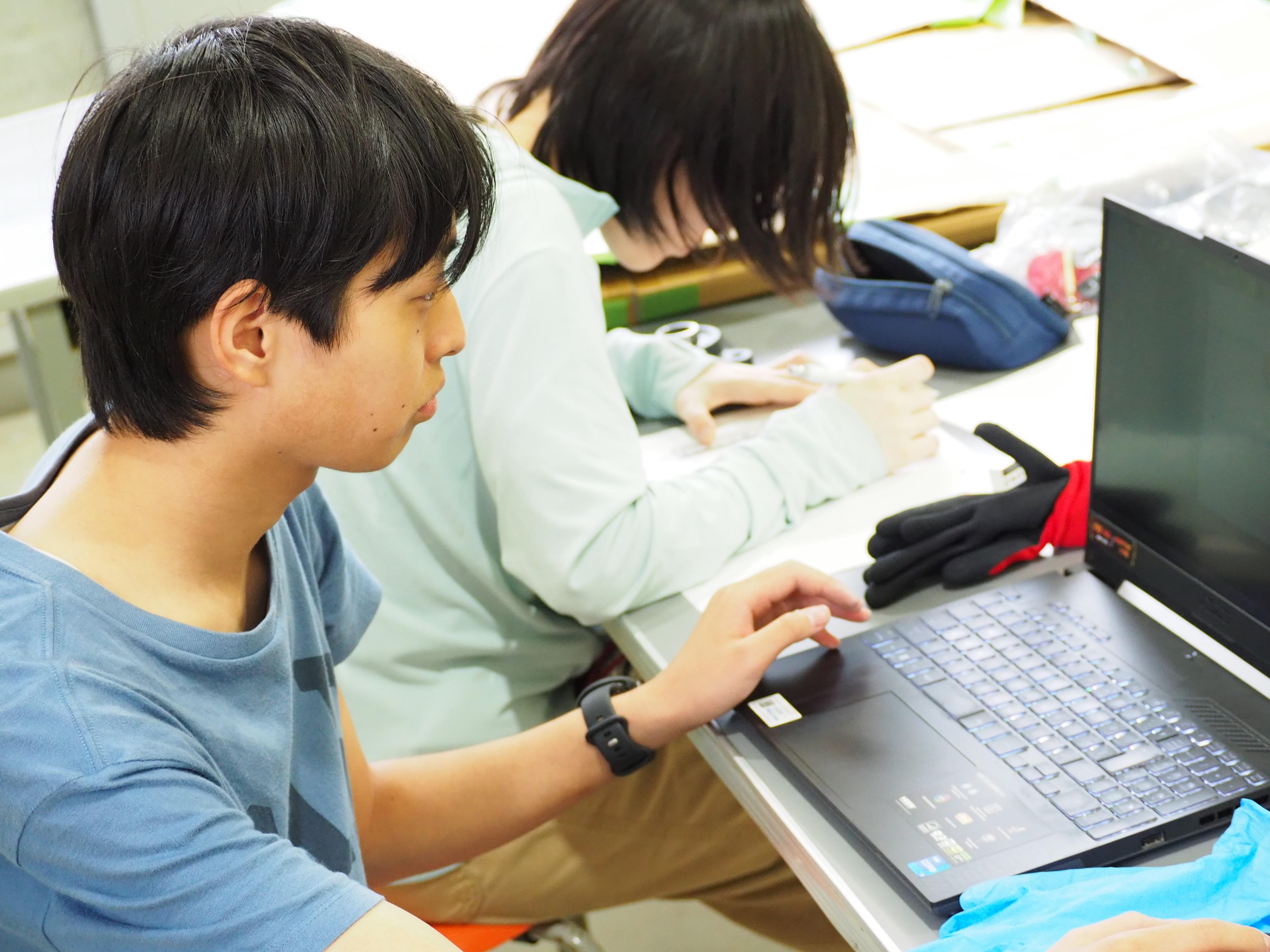 久留米工業大学の学科横断チームの学生たちが、パソコンを操作しながらそれぞれの作業を進めている様子