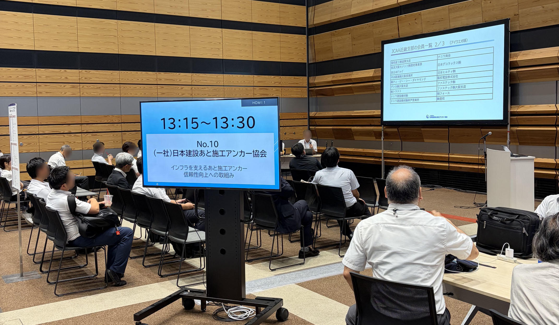 展示会場にて、スライド資料や解説映像が映し出されたモニターを見つめる参加者たちの様子